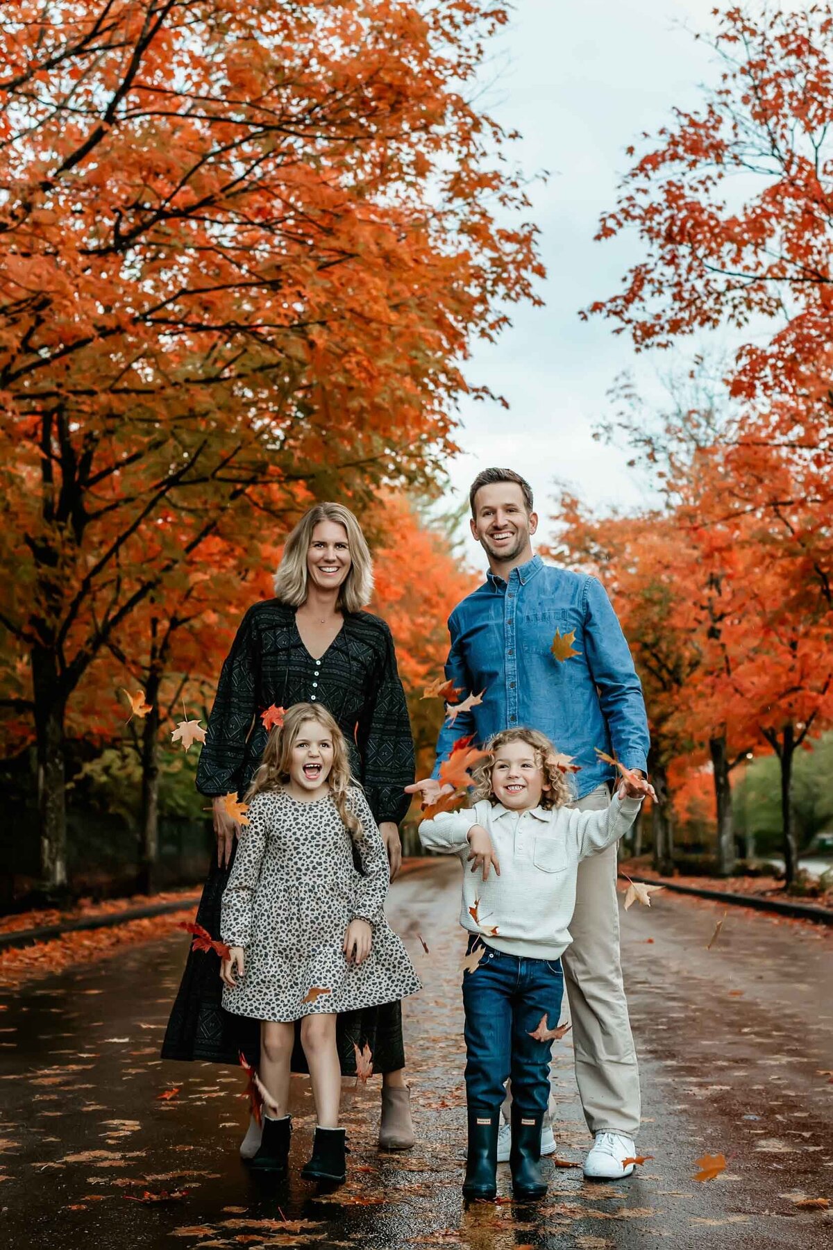 Joyful candid moment of a family tossing fall leaves in the air and laughing together during an autumn photo session.