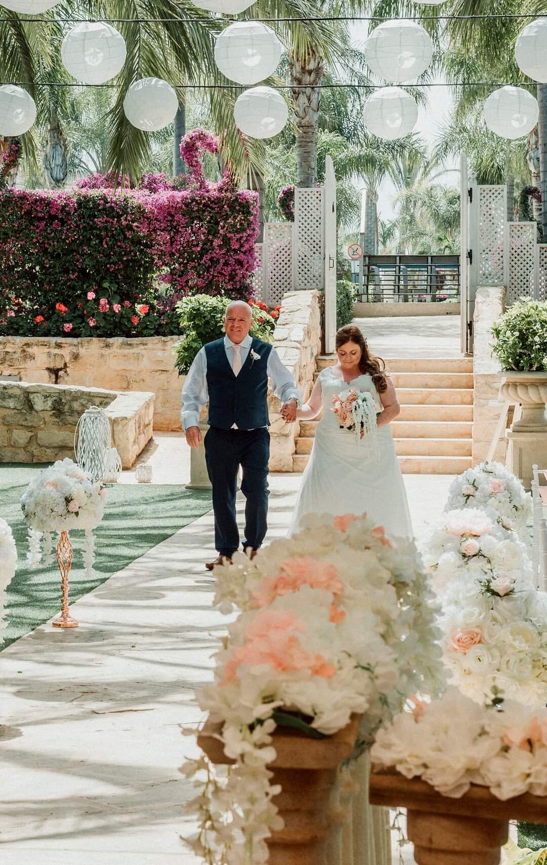 Bride walking with her father down the aisle surrounded by peach and white flowers