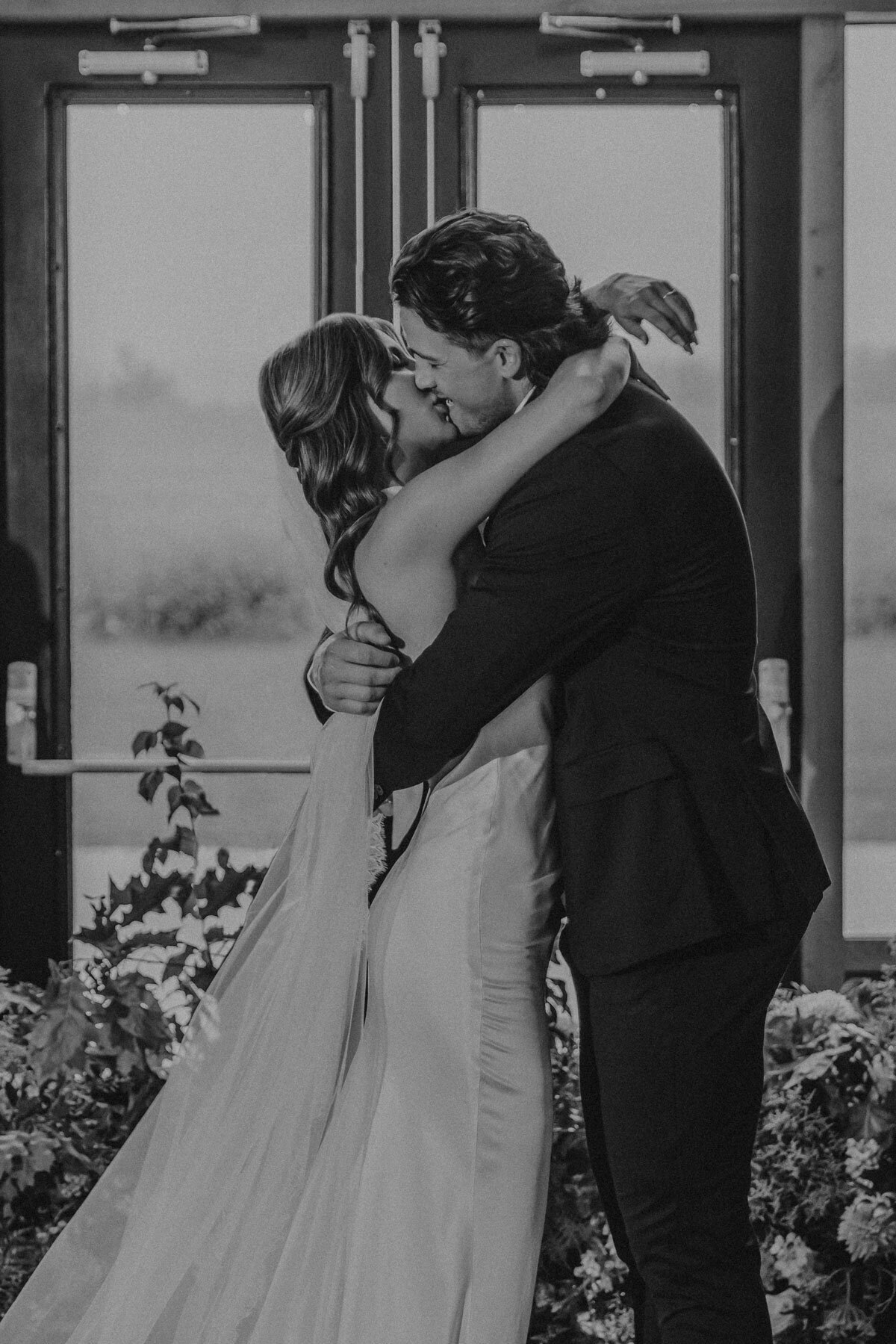 Black and white photo of bride and groom sharing their first kiss as husband and wife.
