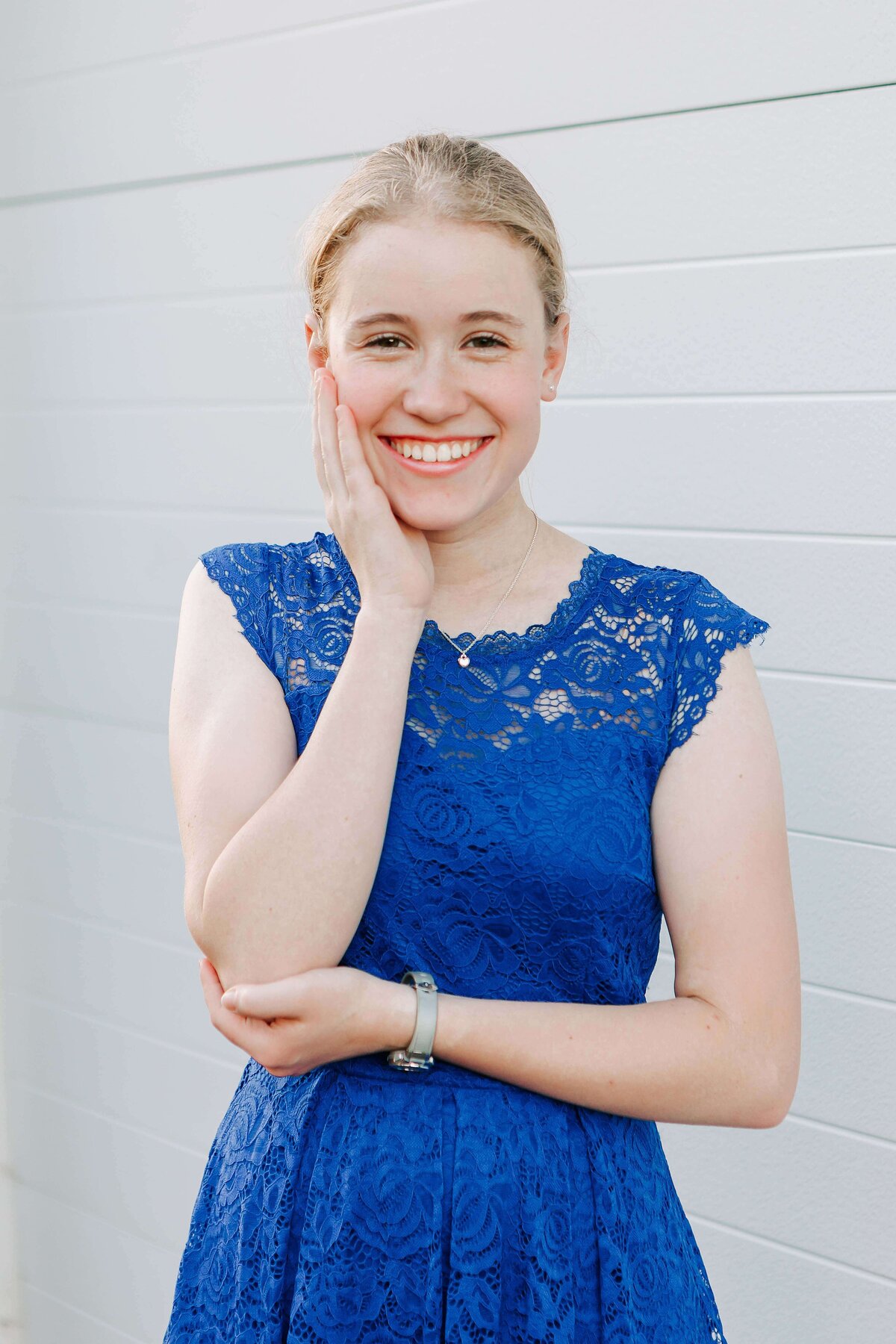 A high school senior in a blue dress stands in front of a white door in Albany, Oregon