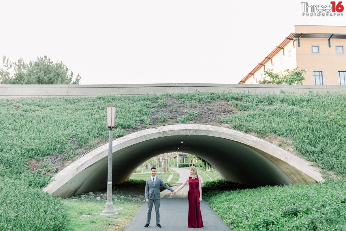 Engaged couple pose holding hands in front of the grass covered tunnel at UC Irvine