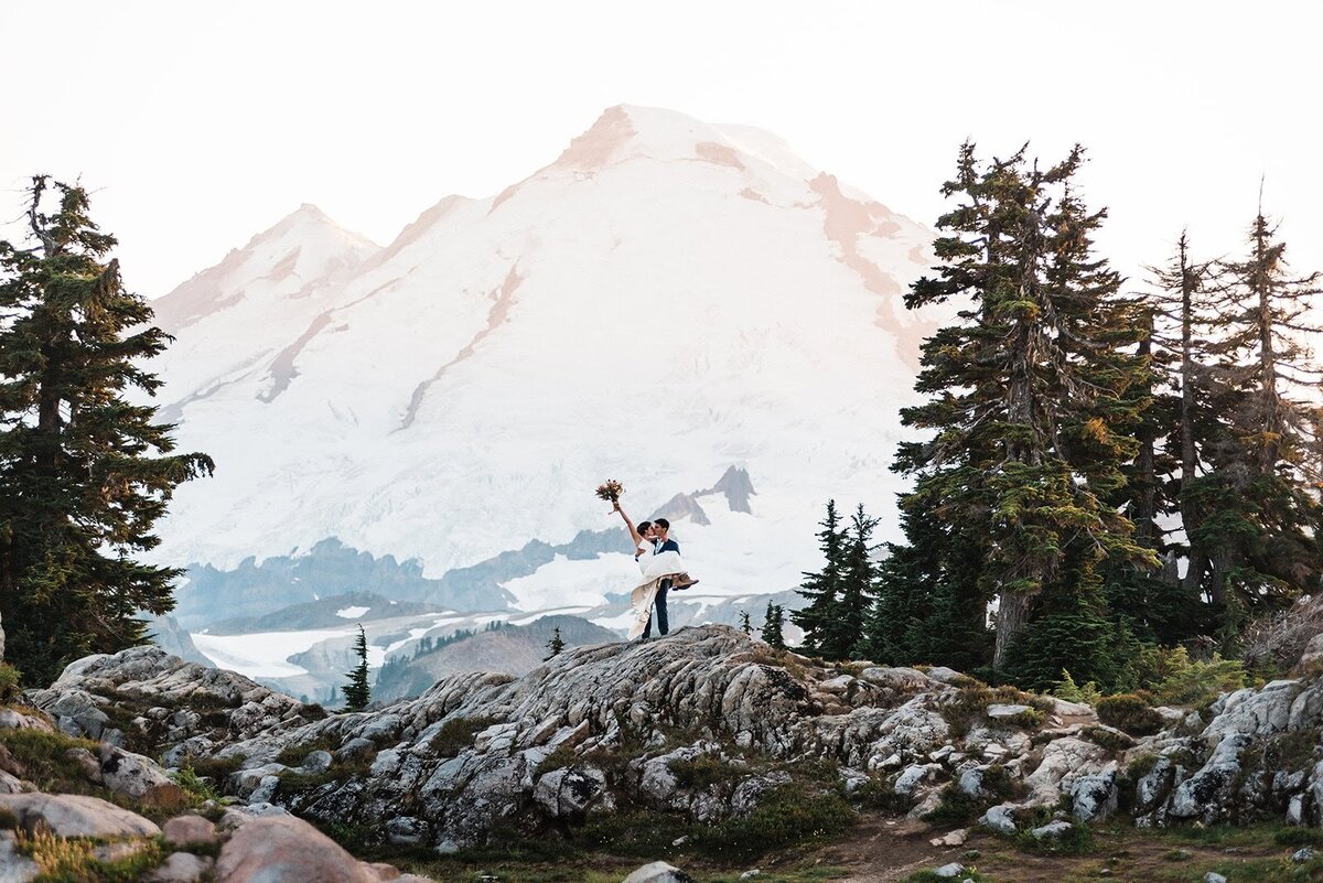 Bride with bouquet in the air being carried by groom in front of Mount Baker in the North Cascades!