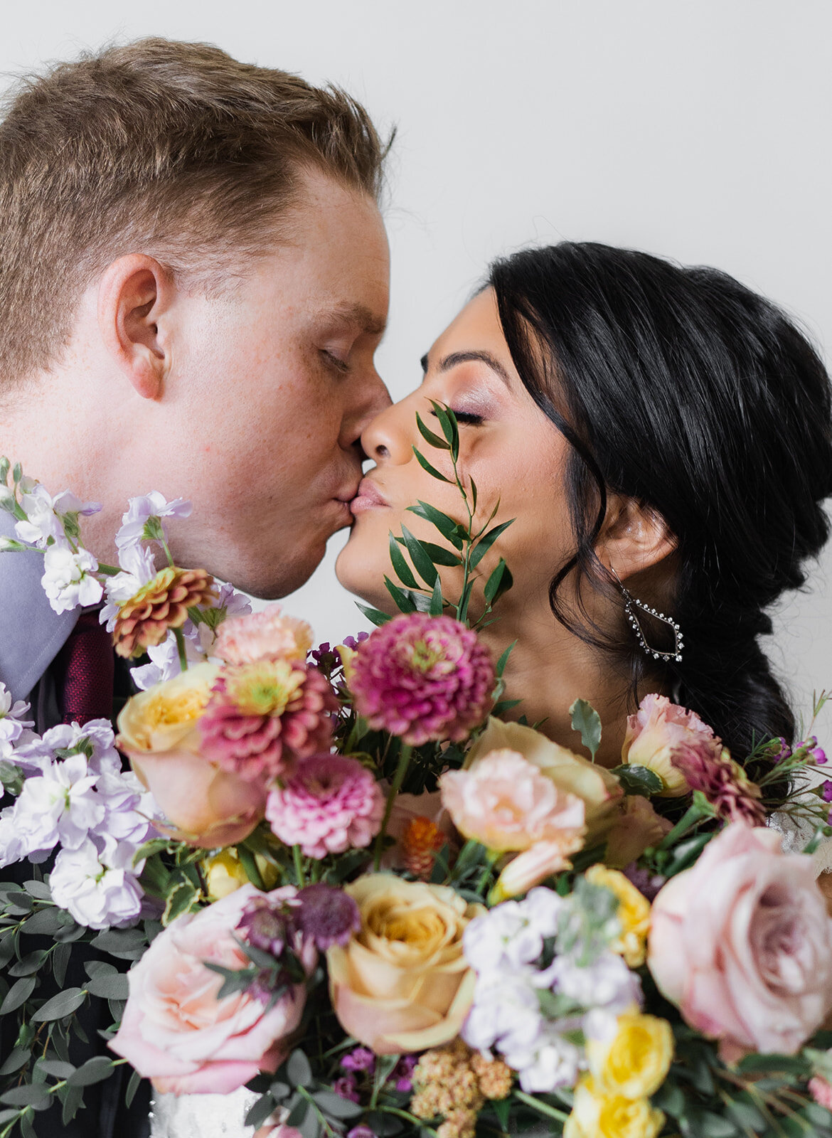 couple kissing behind the bride's bouquet