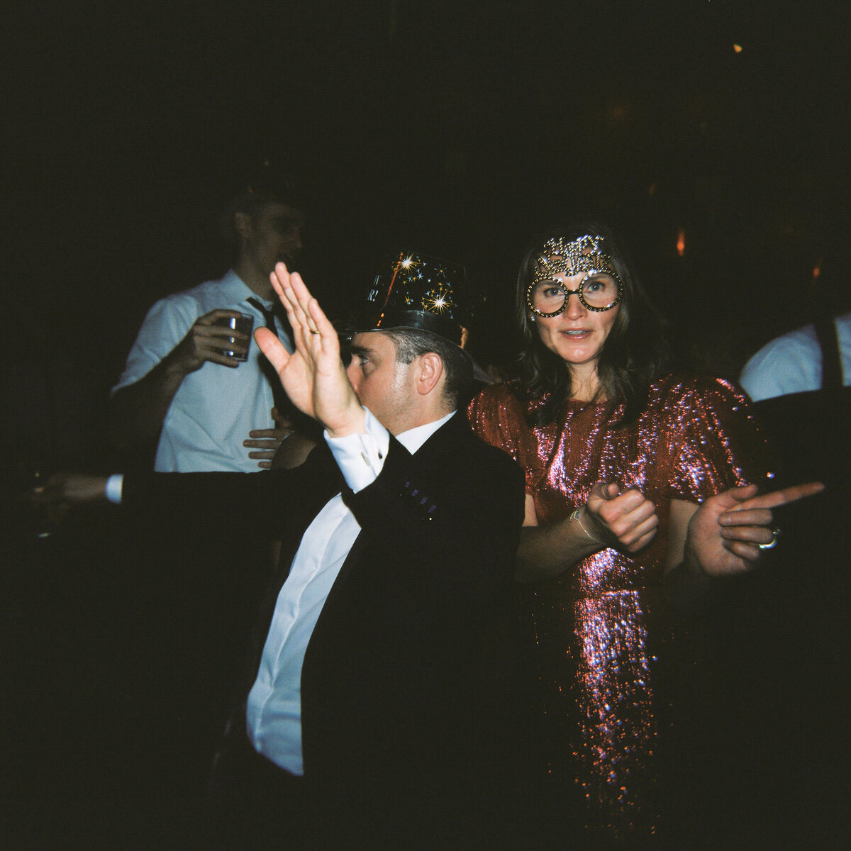 A couple dances enthusiastically at the wedding reception, wearing party hats and shimmering outfits.