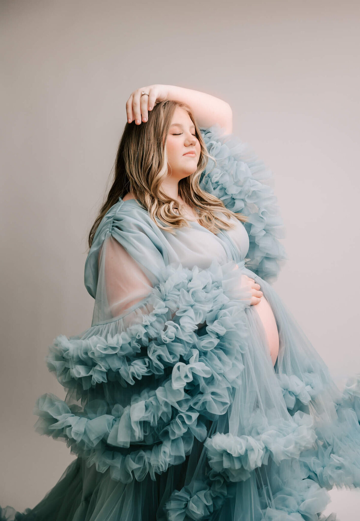pregnant mom with belly showing in blue tulle dress. She has her eyes closed