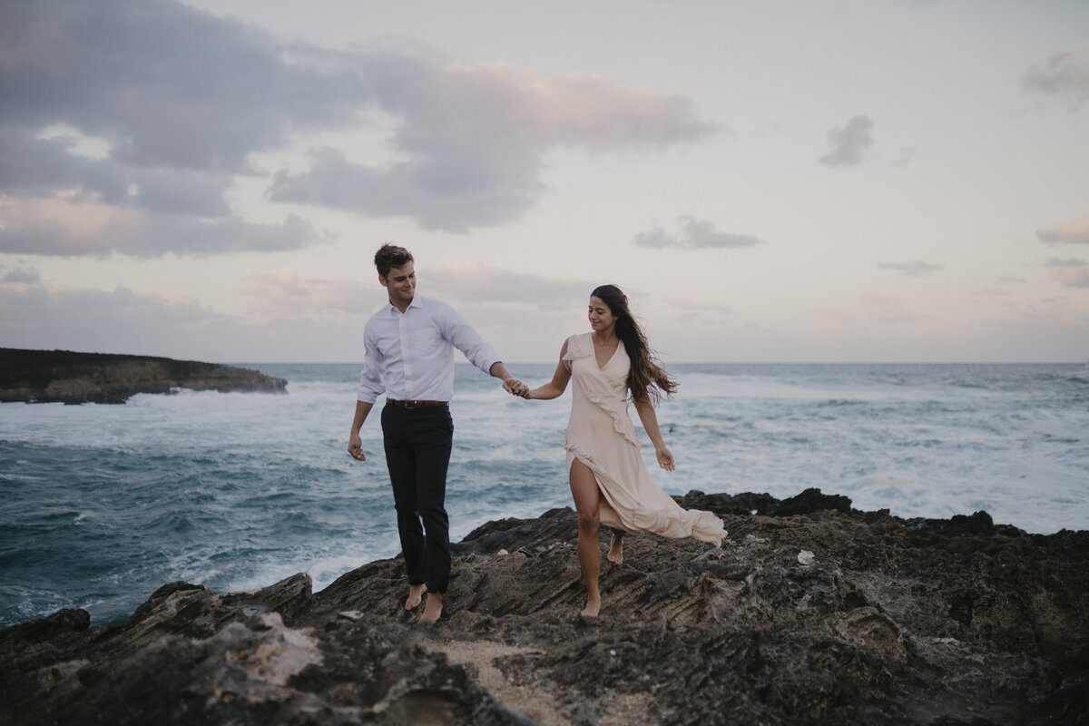 Couple holding hands and standing on the rocks off the ocean