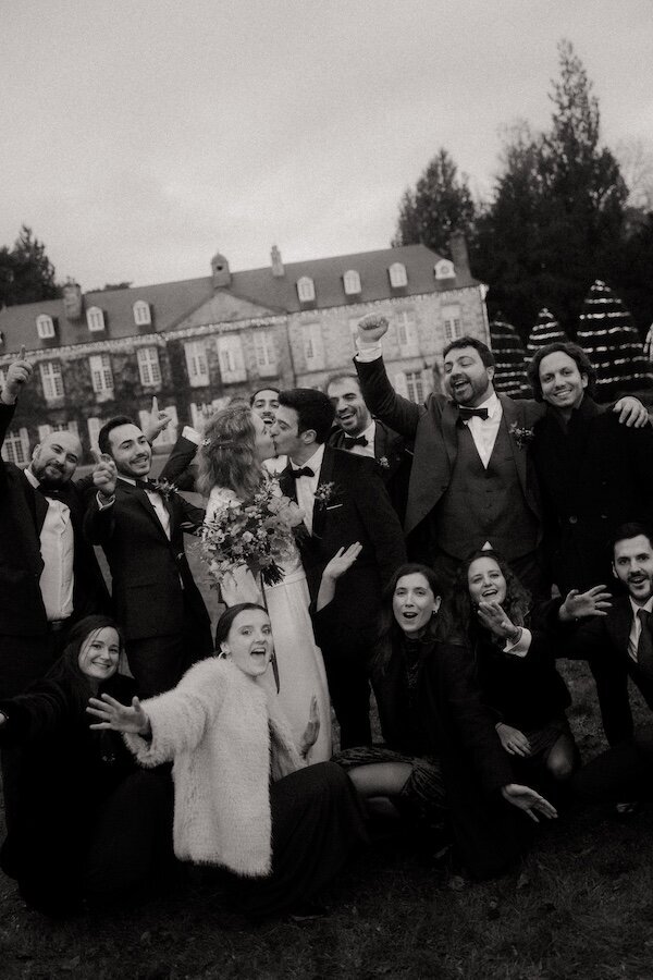 Mariés entourés de leurs proches pour une photo de groupe en noir et blanc devant le château de la Rouerie en Bretagne. Reportage Kamescop, photographe et vidéaste mariage vintage.
