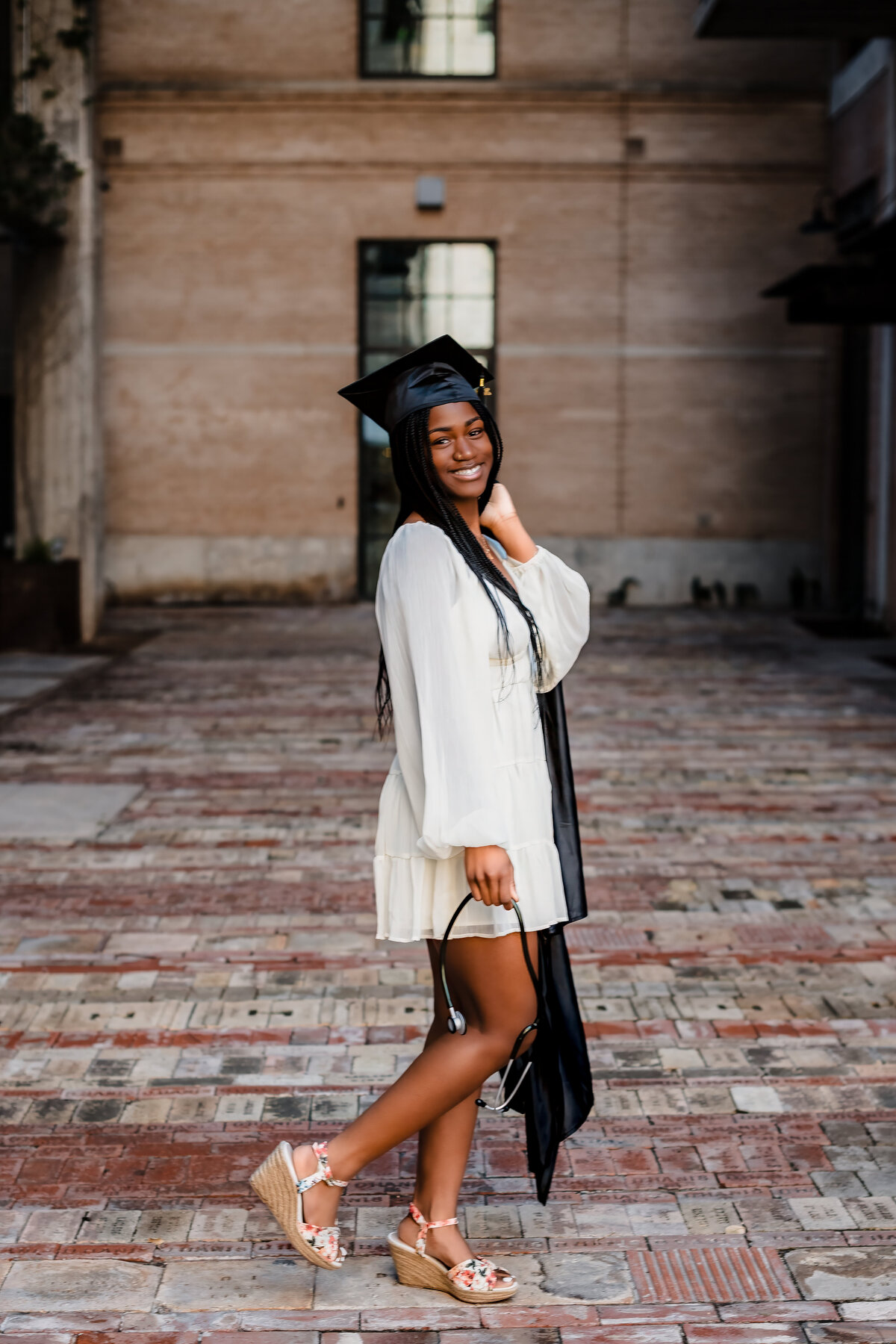 teel High School senior girl holding stethoscope while wearing white dress and black gown at The Pearl.