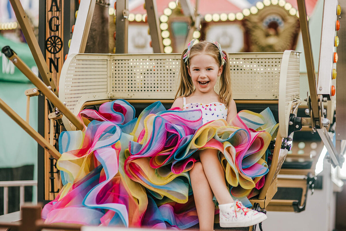 Girl in a rainbow dress and pigtails smiling and sitting on a ferris wheel at a carnival near Annapolis Maryland