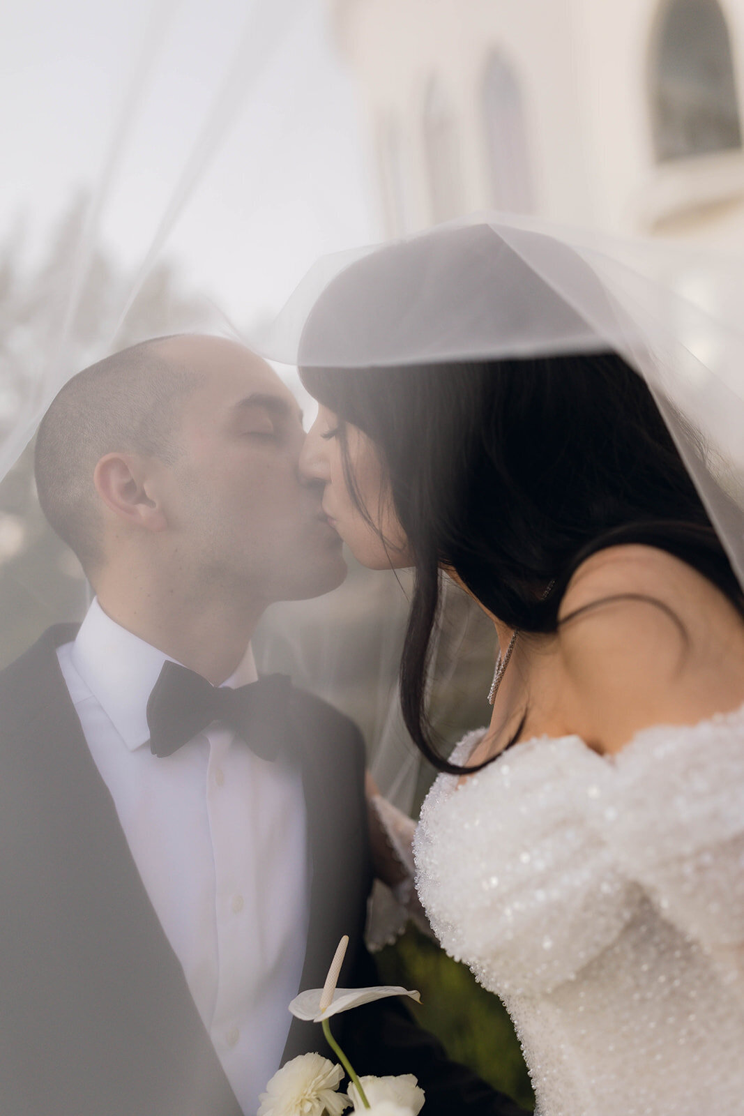 A romantic wedding portrait of a bride and groom sharing a kiss beneath the bride’s veil, capturing an intimate and dreamy moment.