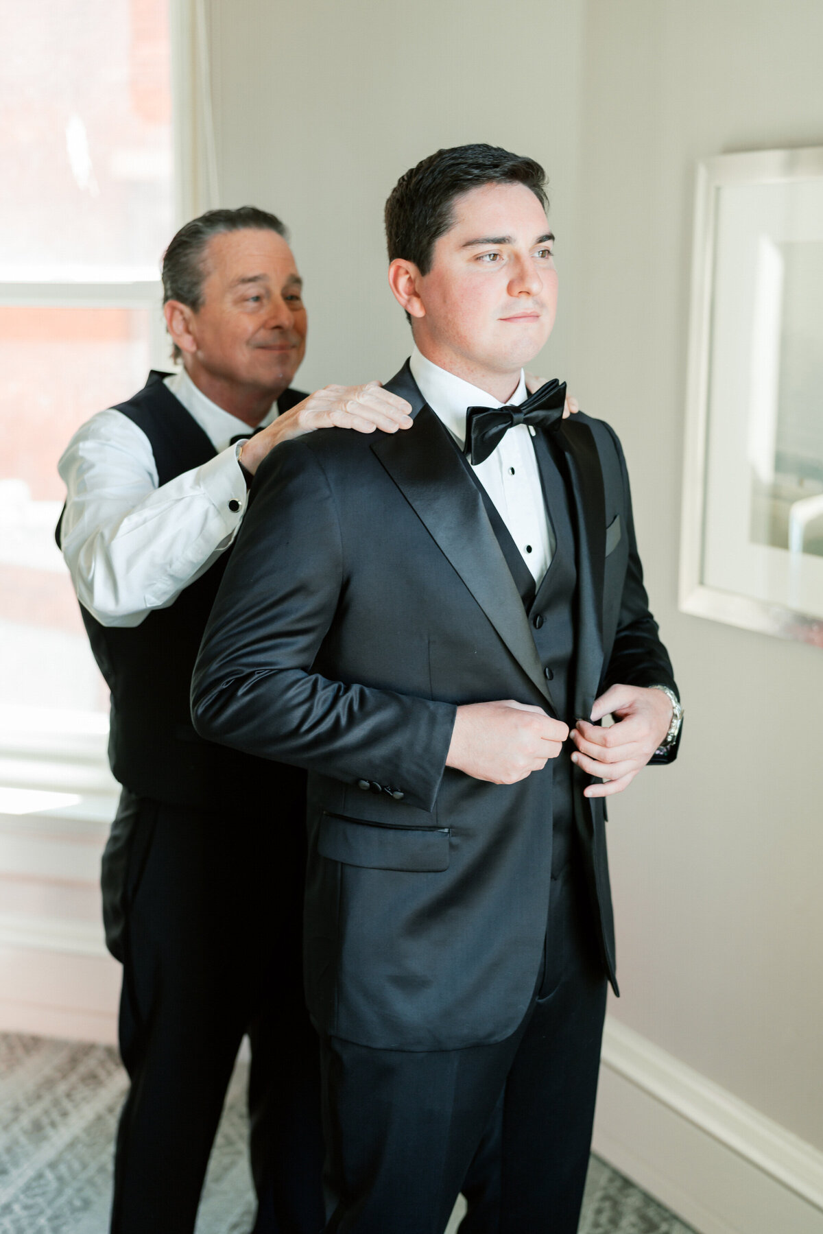 Groom receives help from father while buttoning tux, emotional wedding moment by Philadelphia photographer.