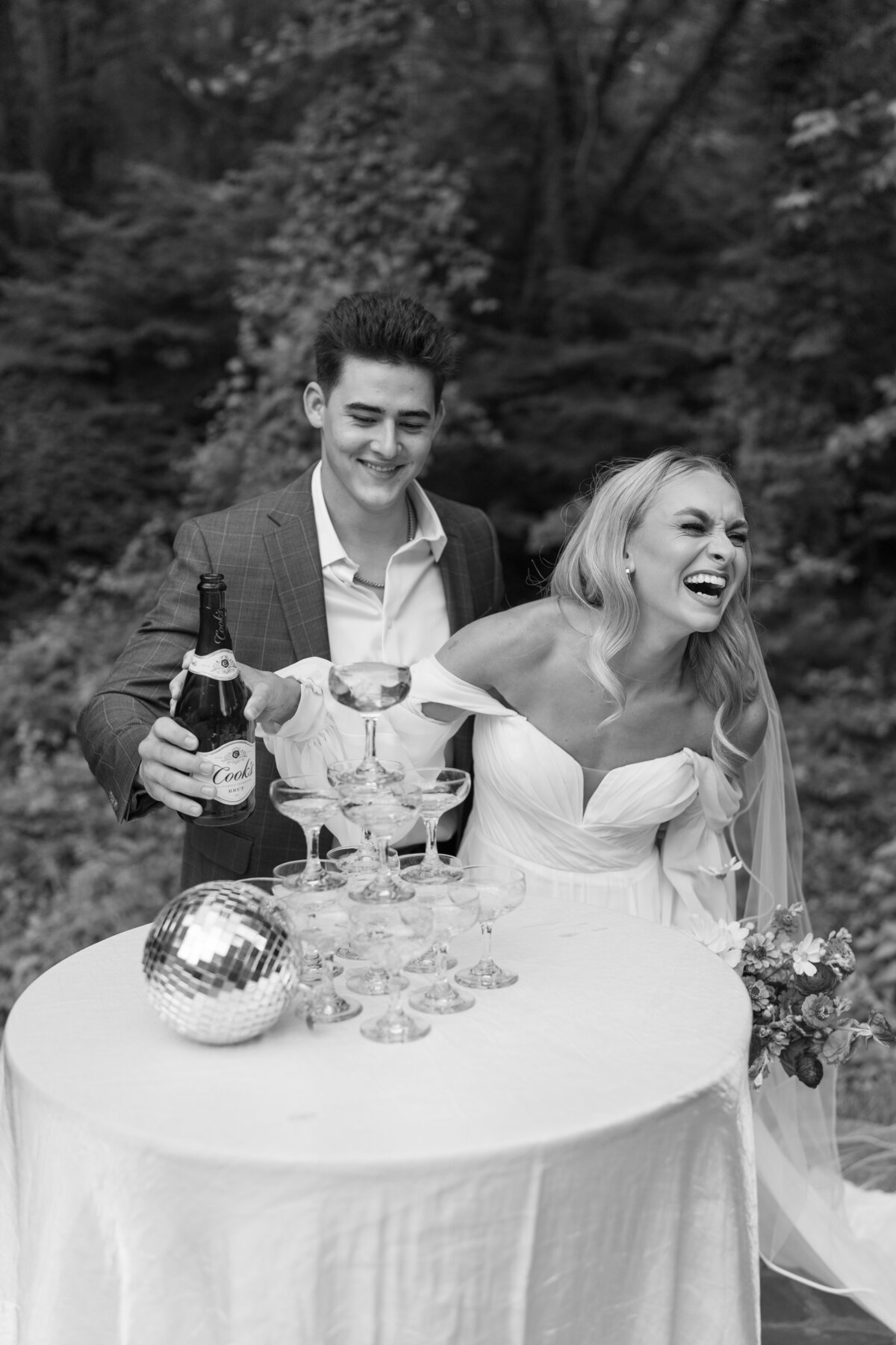 Couple popping champagne during their wedding reception, laughing with friends and family.