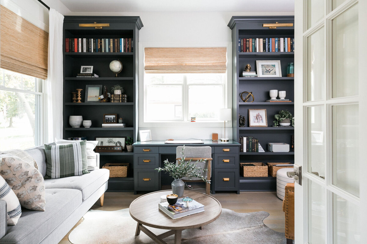 Modern coastal home office with navy blue built ins, desk, and seating area.