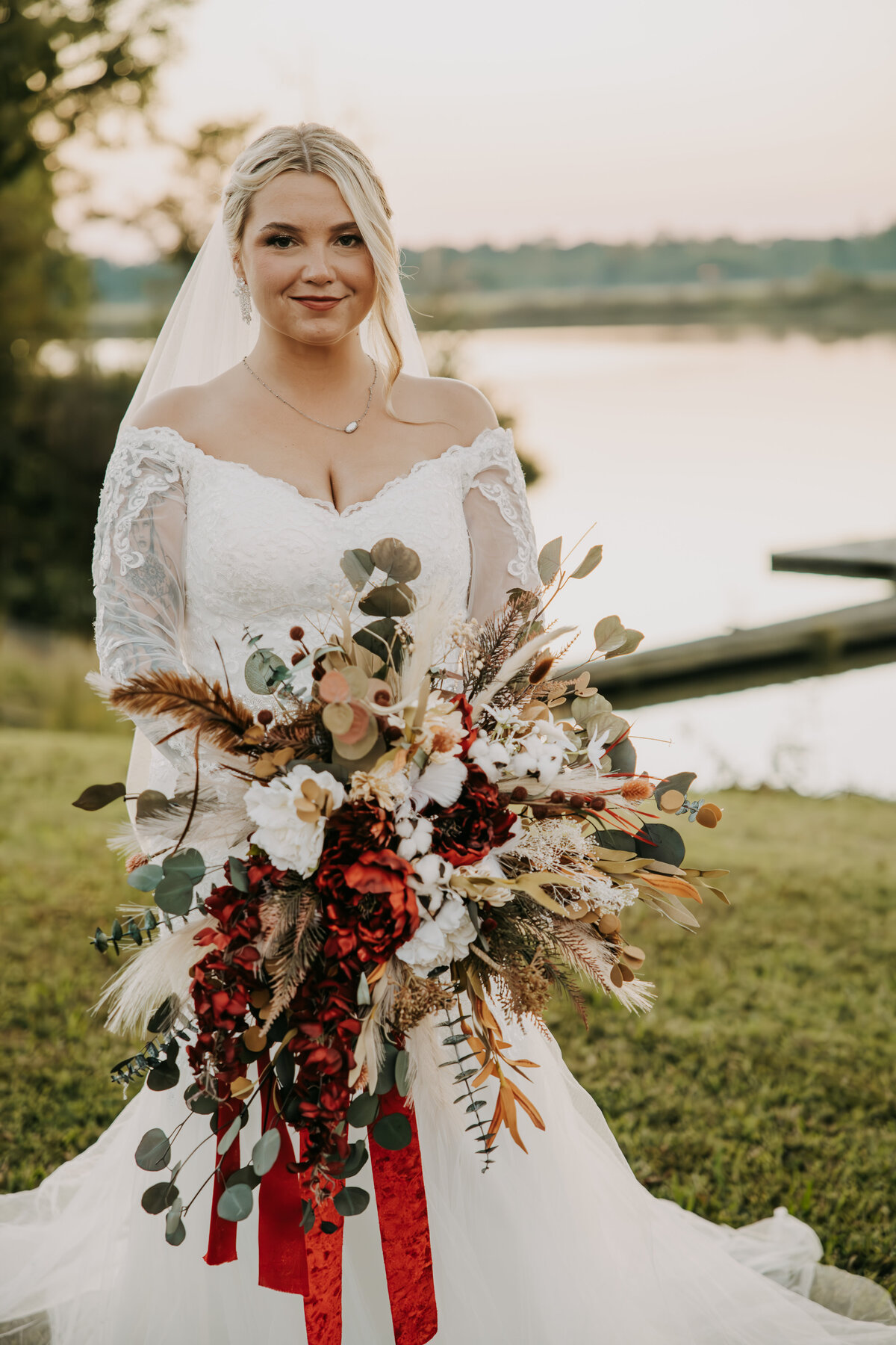 Bride standing in front of a pond at Navy Lakes in Millington, Tennessee, holding a fall-colored bouquet and looking at the camera."