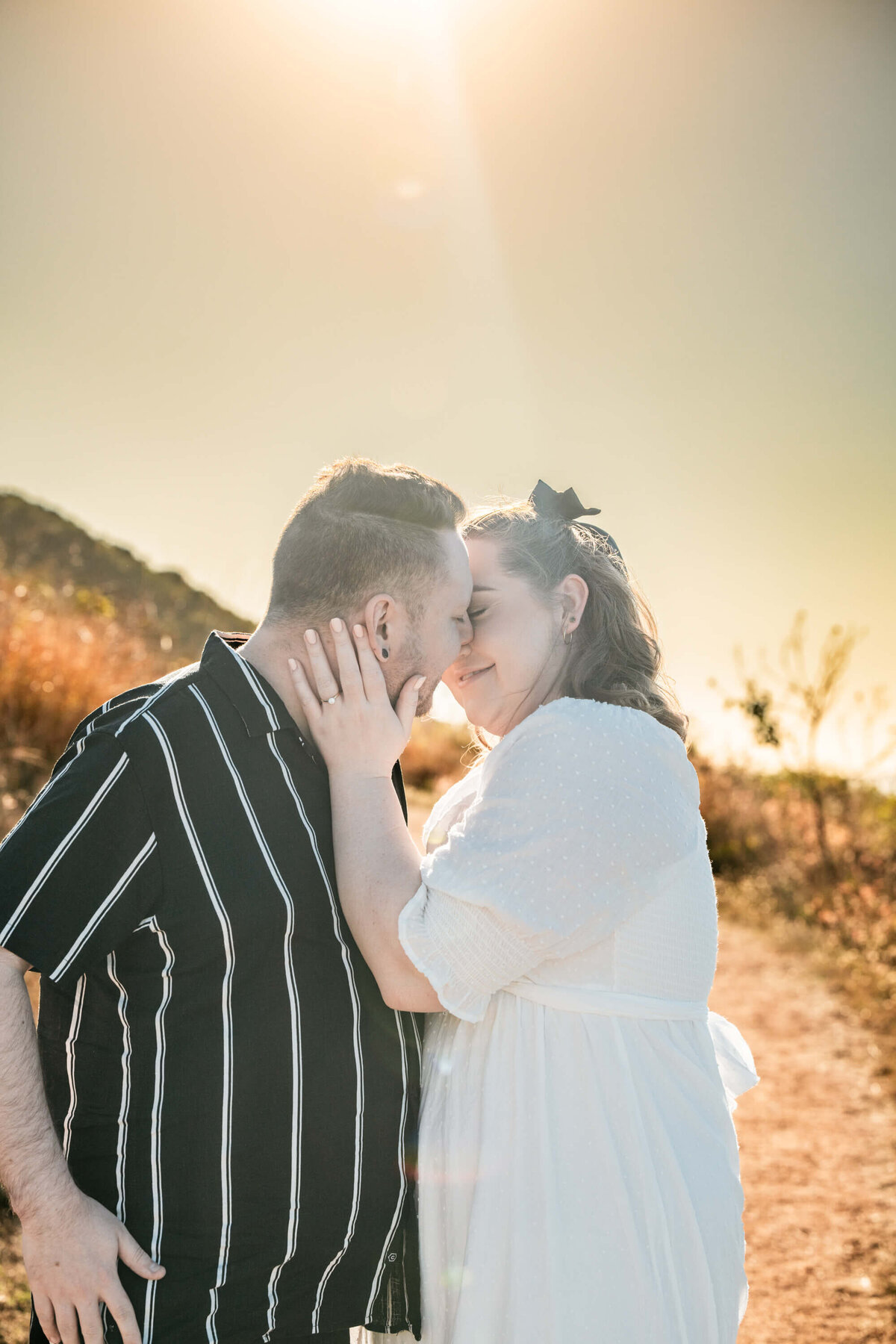 A couple shares a romantic kiss in the sunlight during their engagement session, capturing a moment of love and joy.  - photo by Jamie Simmons