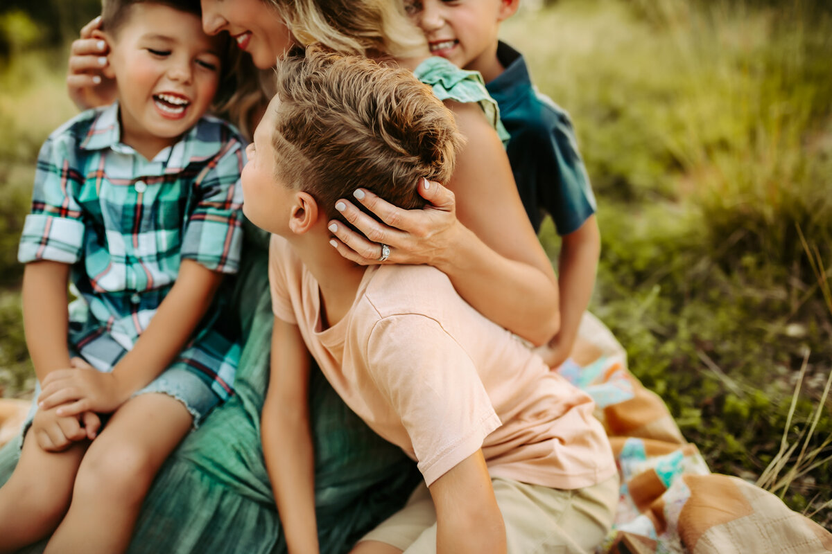 Mother embraces her three sons while they laugh and giggle in her arms