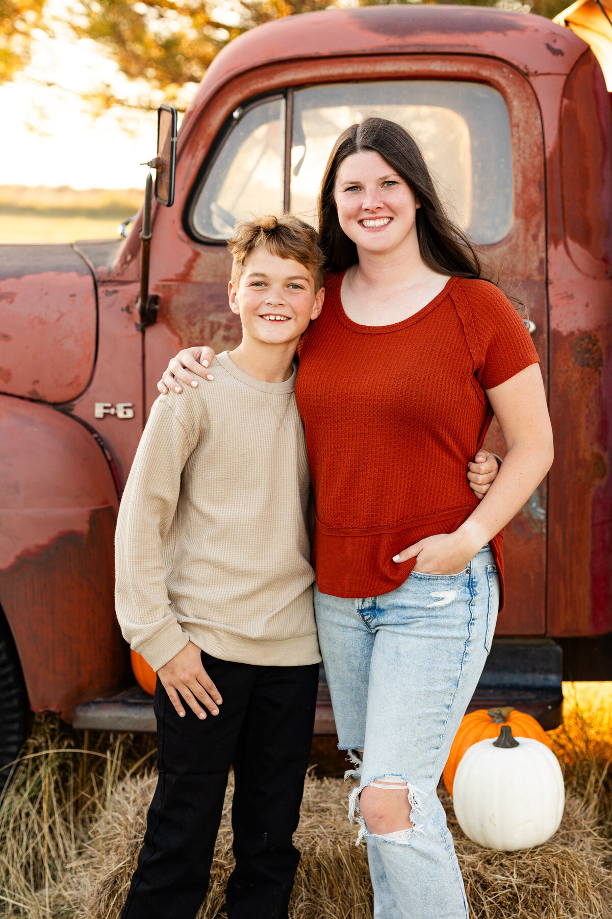 Mom and preteen boy stand with arms around each other's shoulders and smile at the camera.