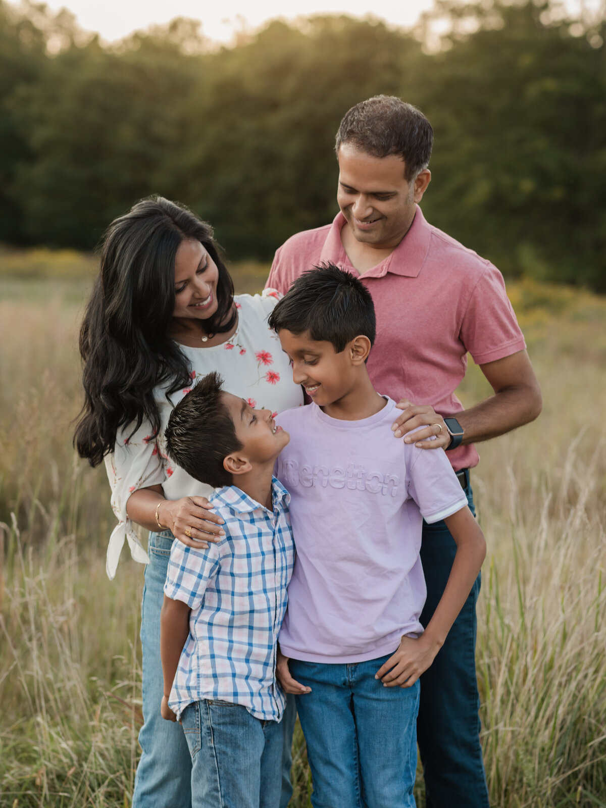 mom dad and two sons posing in field for family photos