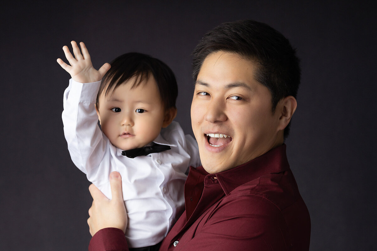Dallas baby photographer captures a joyful moment with father and son, dressed in matching tuxedos and sharing a playful smile.