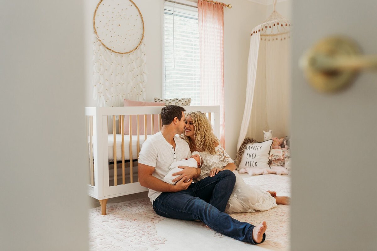 parents kiss holding baby in newborn room