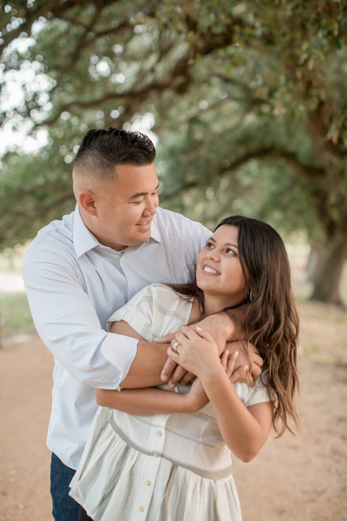 An engaged couple look at each other while the man embraces his fiancee from behind