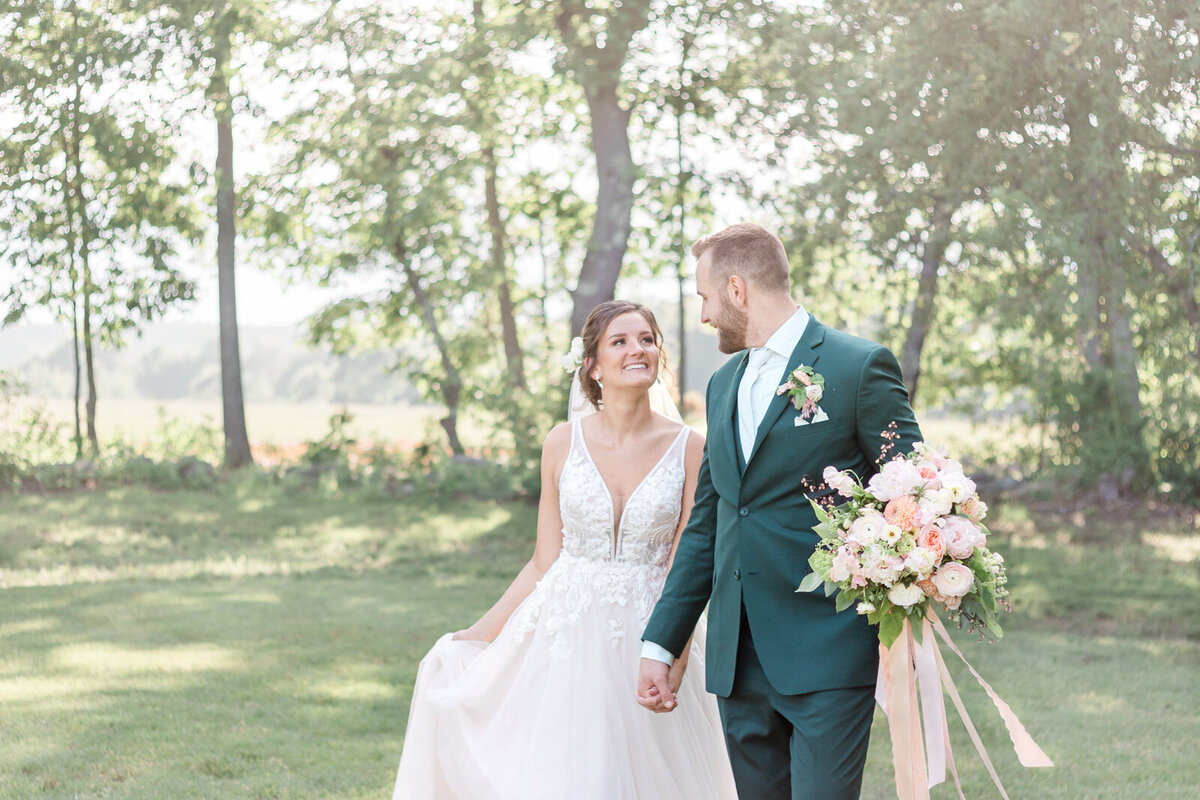 A bride and groom walk hand in hand through a field in New hampshire on their wedding day