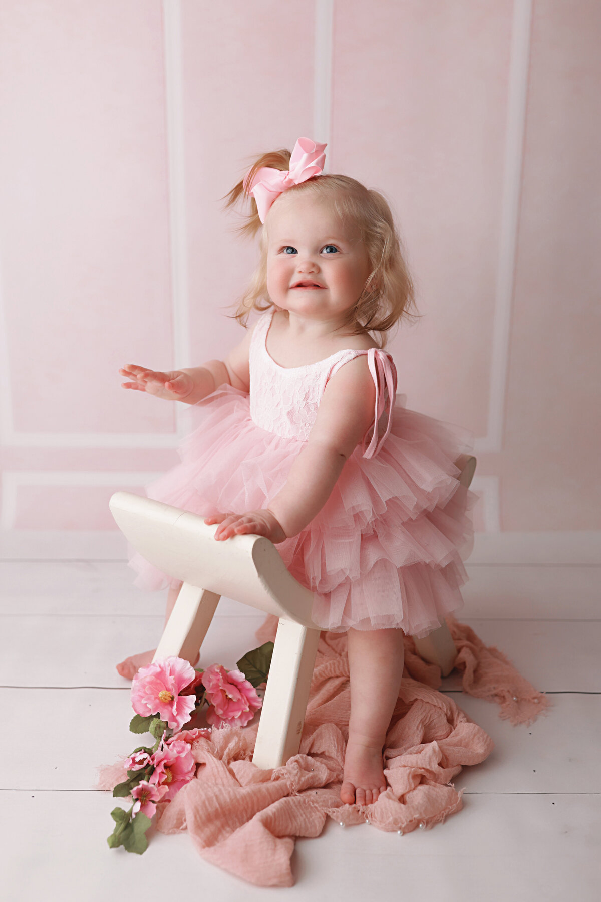 baby girl sitting on a white stool during her birthday photo session