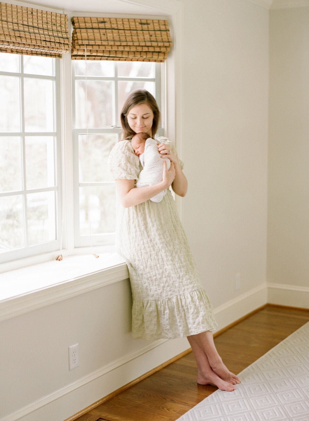 Mom leans in a window and holds her newborn during a Charlotte photography session. Image by Raleigh newborn photographer A.J. Dunlap Photography.