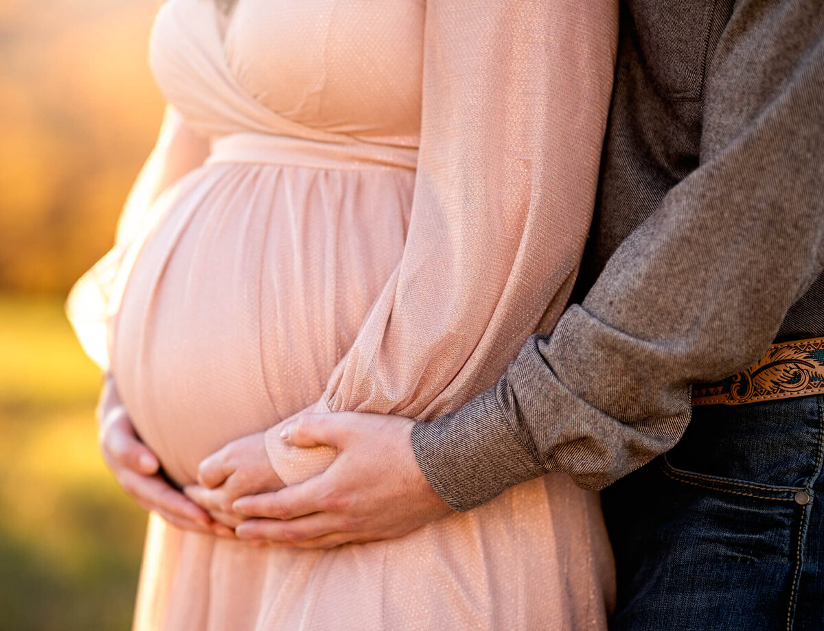 An expecting mama to be and her husband cradle the baby bump