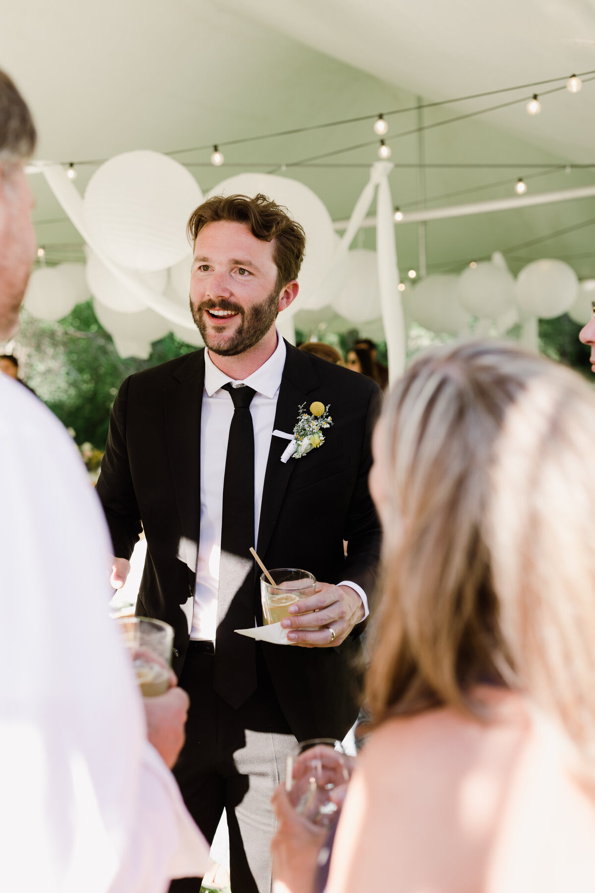 Groom holding a drink whilst chatting to guests