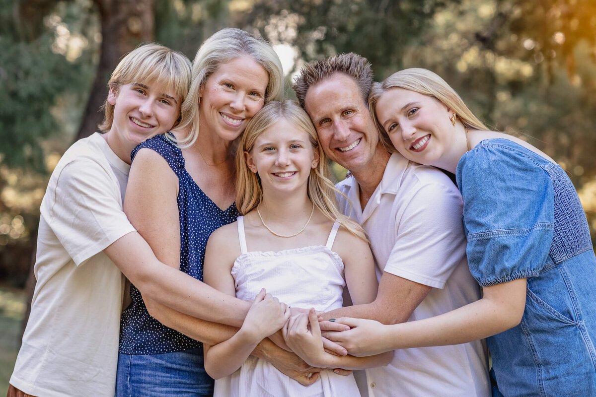 A family of five with blonde hair smiling at the camera with their arms around each other with their heads together in Irvine.