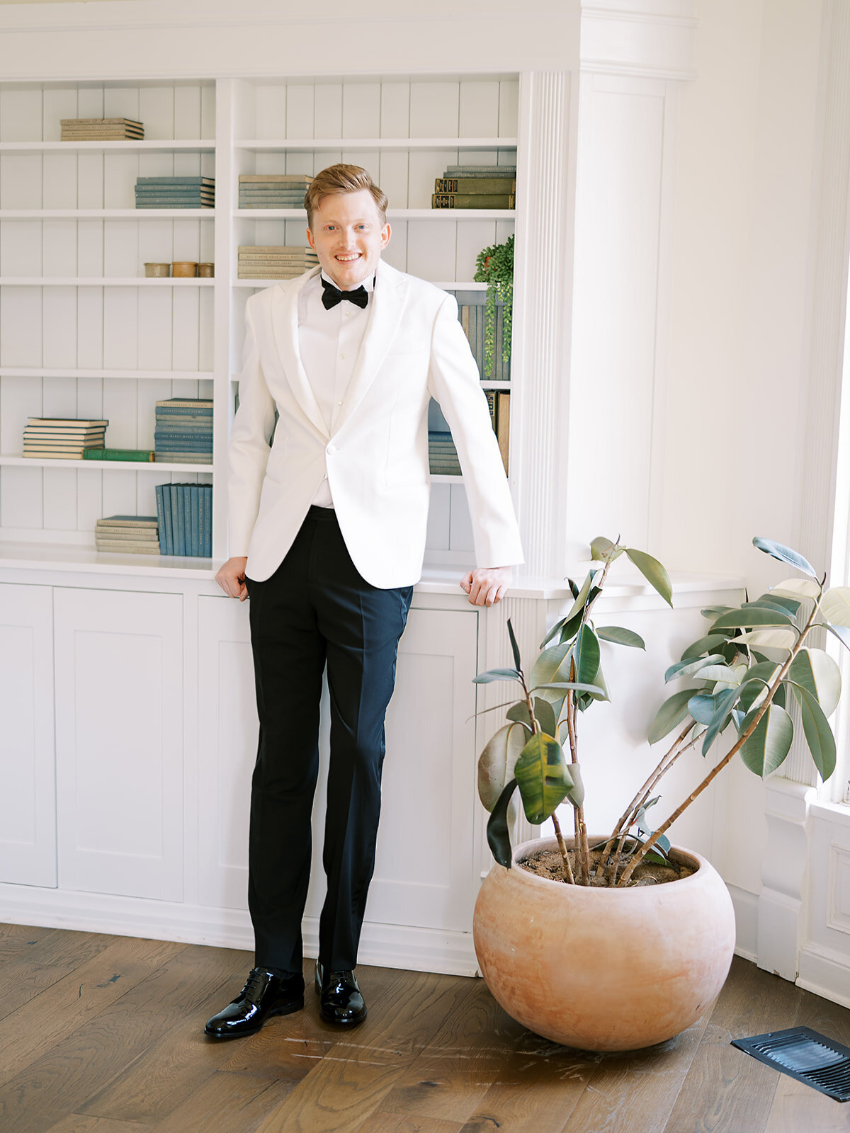The groom poses in front of a bookshelf inside the old home at The Grand Lady