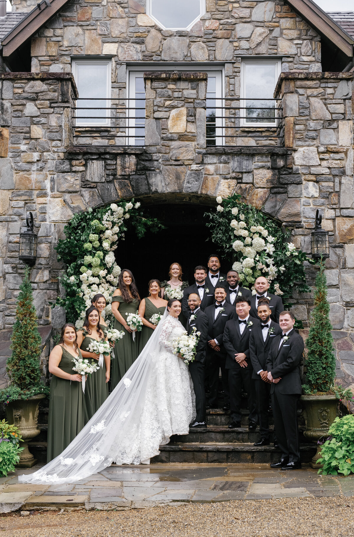 Wedding party gathered on the stone steps of Castle Ladyhawke surrounded by lush white florals and greenery.