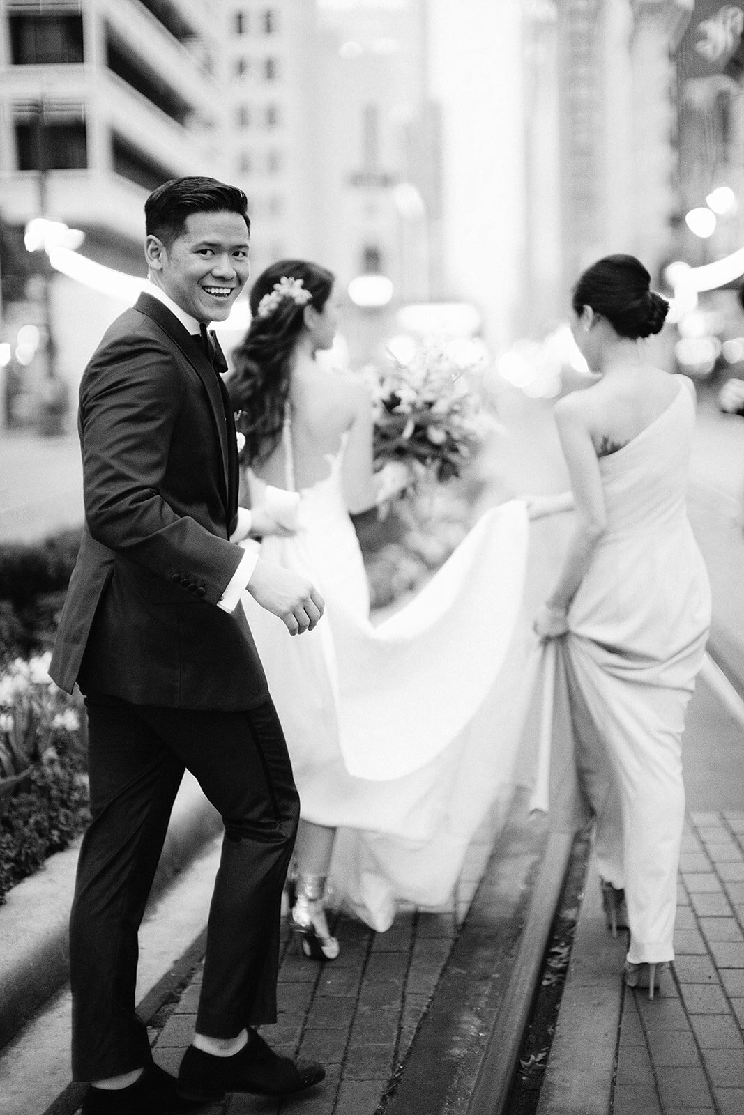 Black and white photo of groom and bridesmaid holding the train of bride's dress
