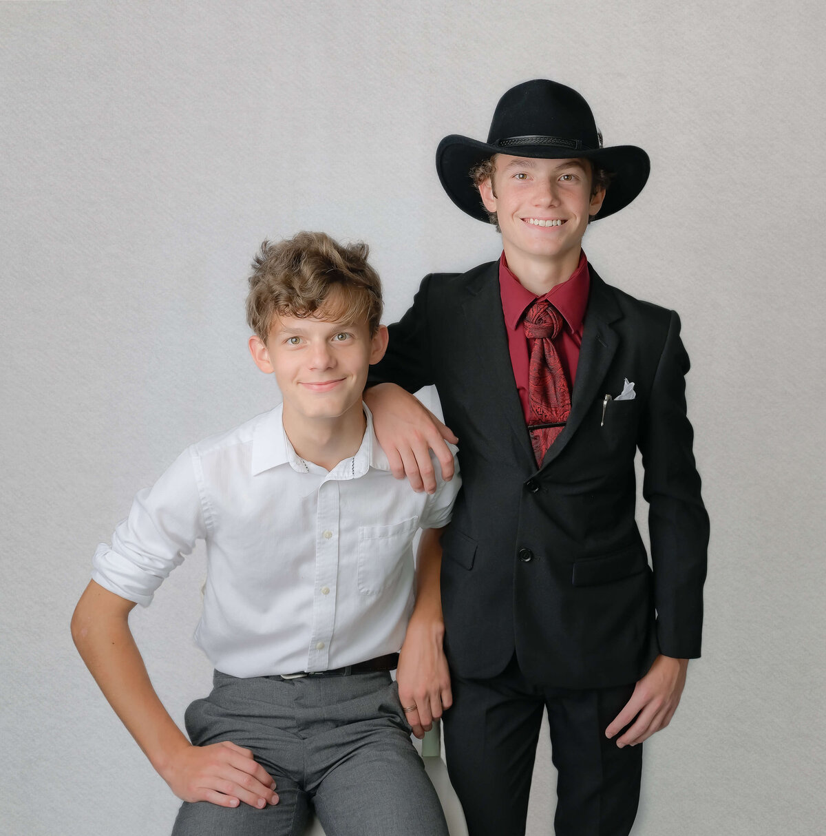 Two brothers in suits pose together in front of a white background during their family photography session in McKinney, TX.