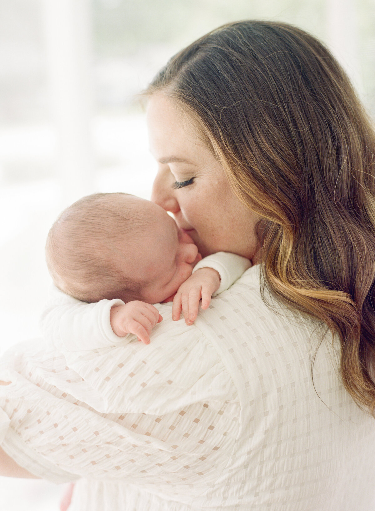 Mom kisses baby on the cheek while he lays asleep on her shoulder during their Raleigh newborn photography session. Photographed by Raleigh newborn photographer A.J. Dunlap Photography.