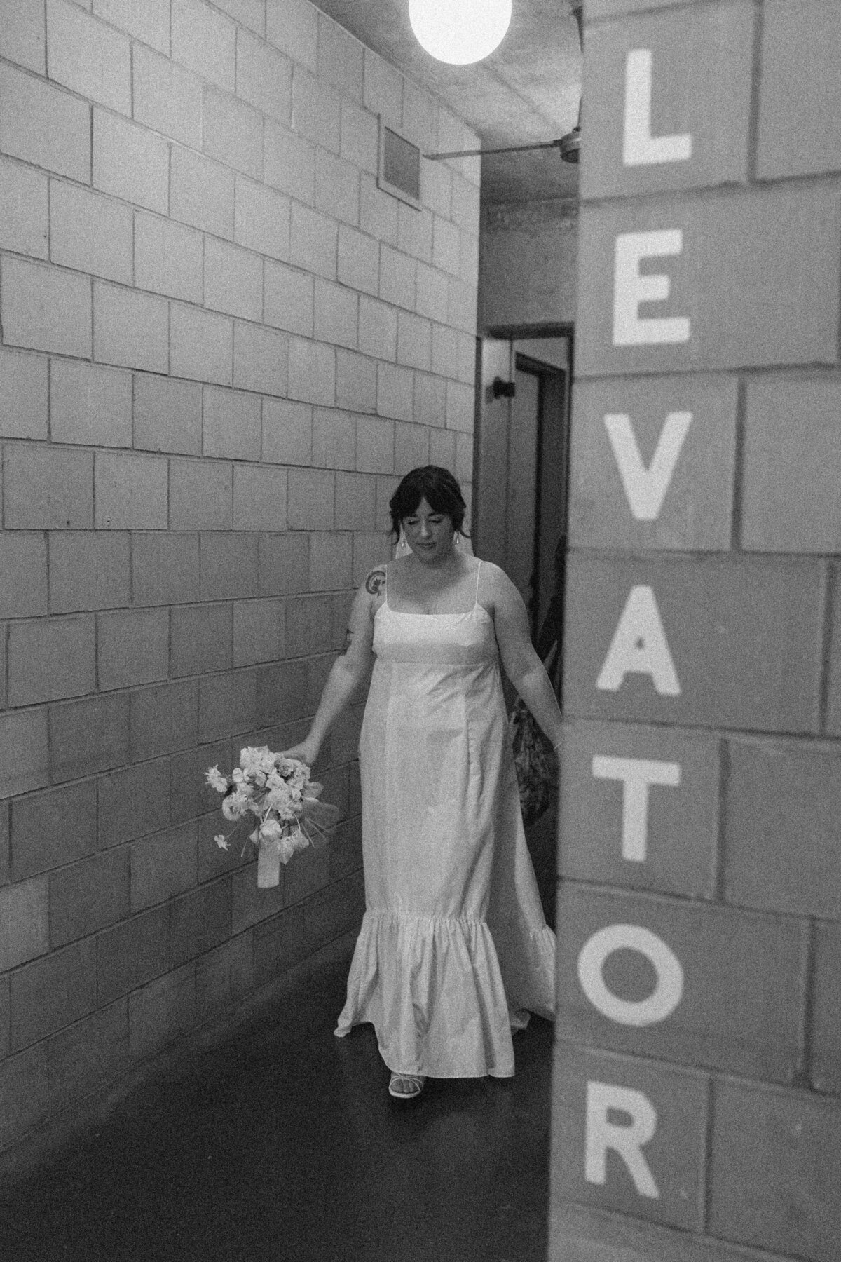 Bride walking through hallway past a sign that says elevator