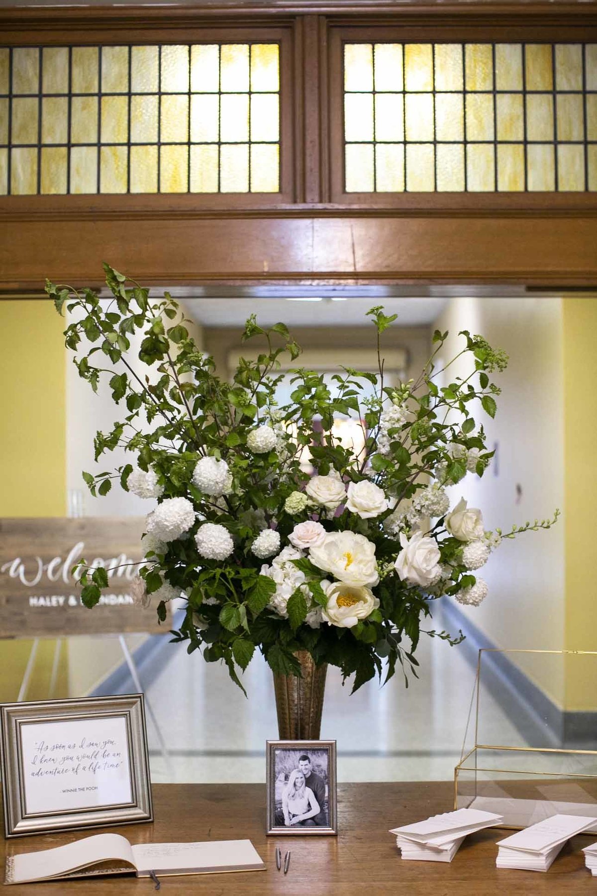 large arrangement of white flowers and tall greenery in gold urn for welcome table