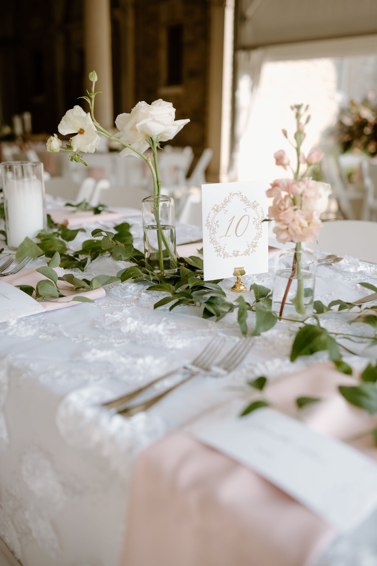 Romantic wedding tablescape with pink florals, greenery, and table number 10.