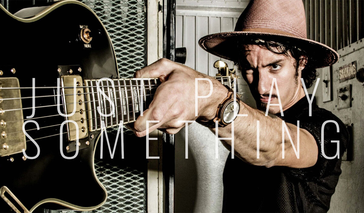 Male musician photo Taylor John Williams wearing black shirt pink cowboy hat holding outstretched black electric guitar while standing inside old elevator