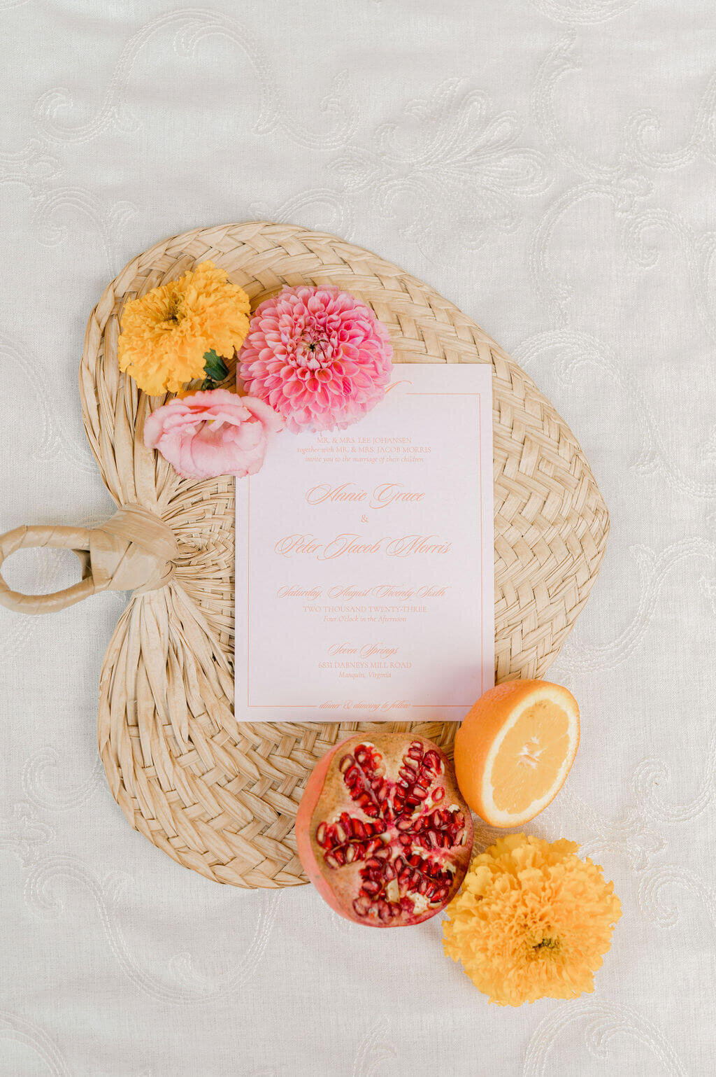 Luxury wedding invitation flat lay with tropical florals and citrus on woven fan. Keywords: wedding day stationery, wedding stationery, luxury wedding invitations, wedding invitation designer.