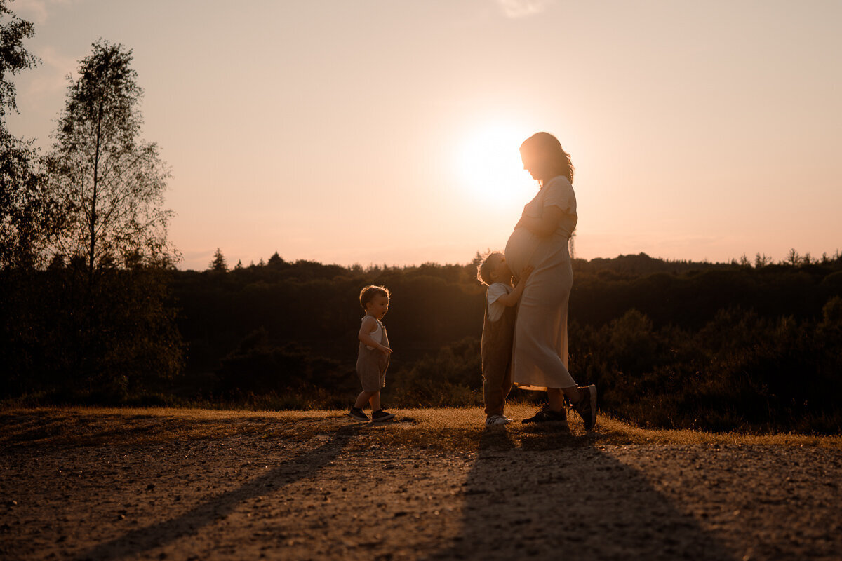 Zwangere moeder krijgt een kus van haar zoontje op haar buik tijdens de zonsondergang