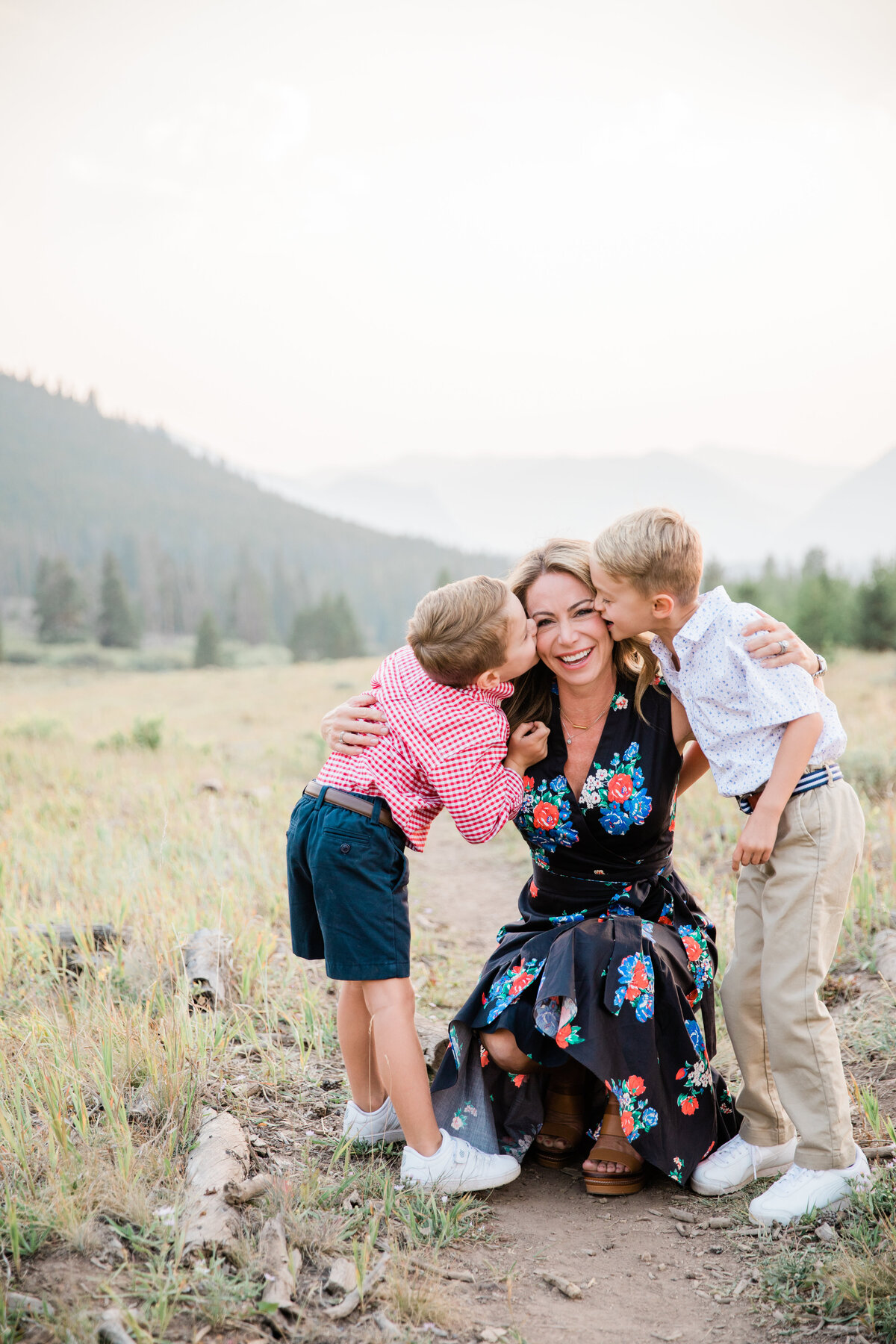 A mom of two boys kneels down to their level to embrace in a hug