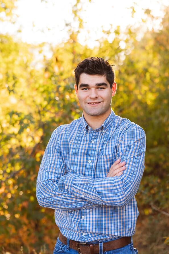 Boy crosses his arms and smiles at camera at a fall park.