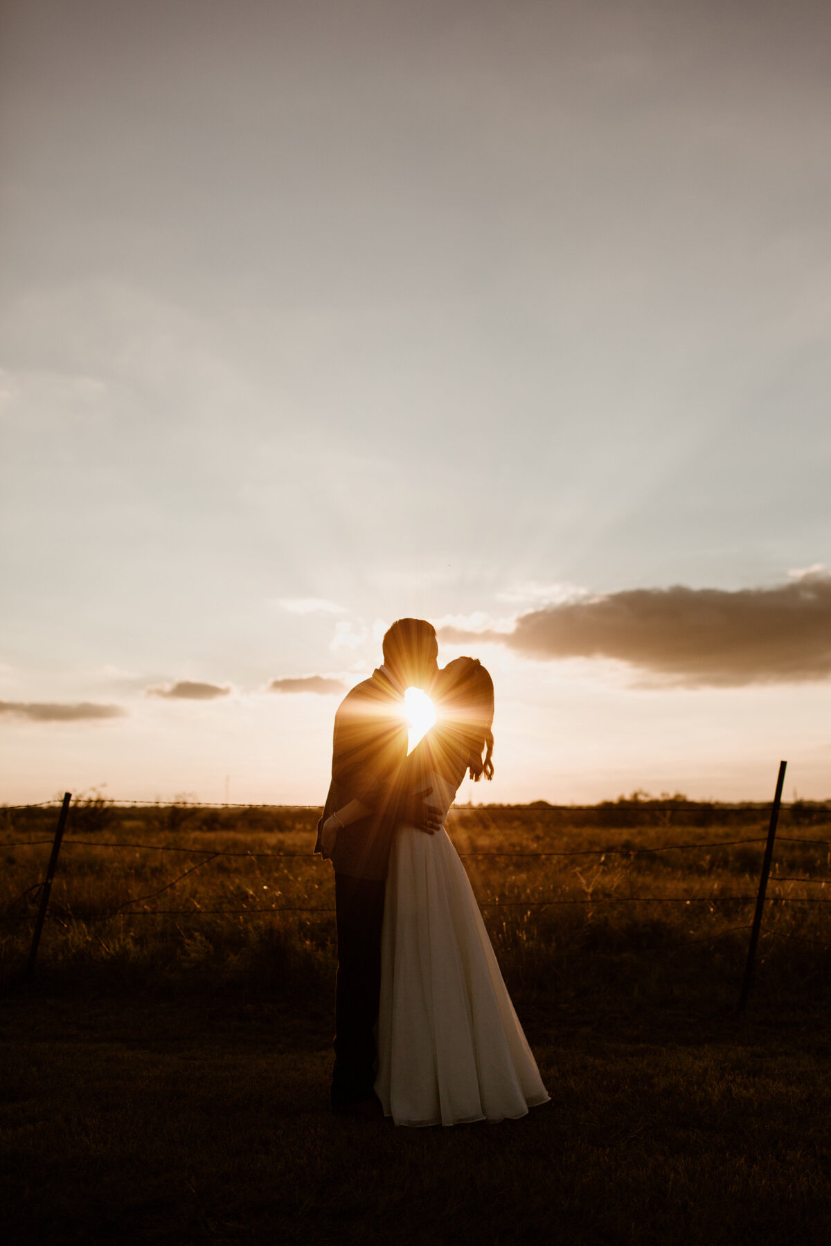 A couple kisses with the glow of the sunset in the background at Chapel Creek Ranch in Denton Texas. Captured by Fort Worth Wedding Photographer, Megan Christine Studio