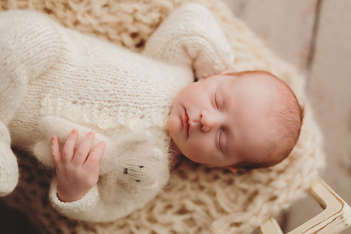 baby boy laying with one hand behind his head and the other holding a small bear stuffed animal