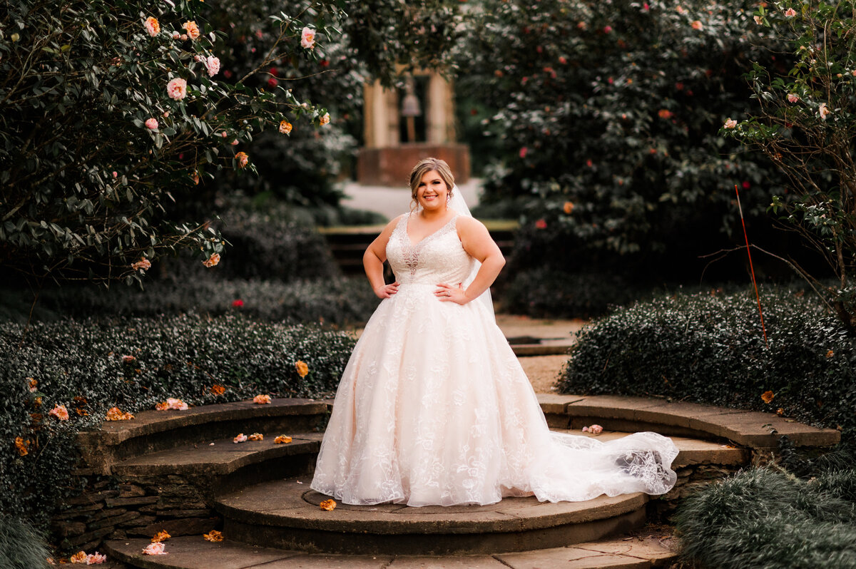 garden bridals with bride standing with her hands on her hips and smiling at the camera with flowering trees surrounding her