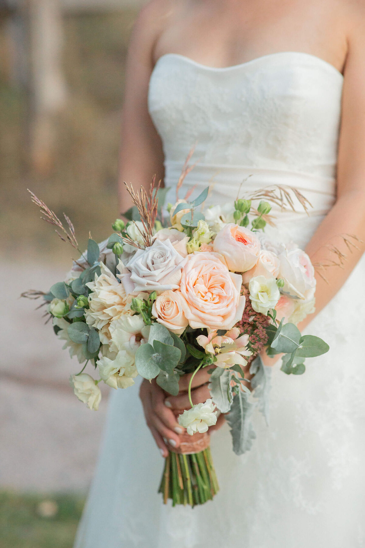 bride shown from the shoulders down in a strapless dress holds her bridal bouquet