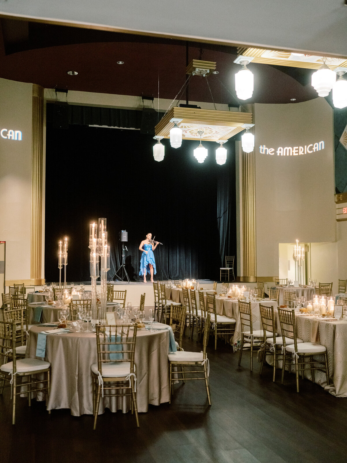 Stunning wedding reception setup featuring tables, candles, and a violinist performing on stage, creating a magical atmosphere for guests to enjoy.