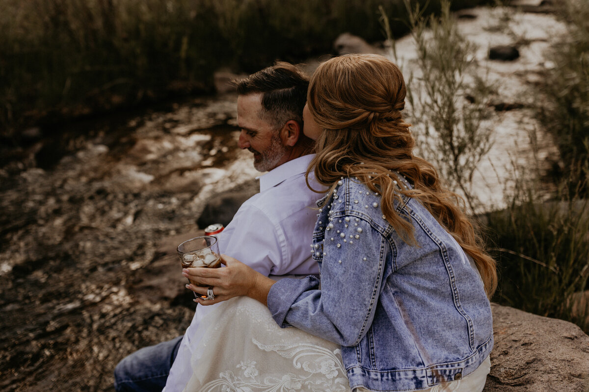 newlyweds enjoying a drink together sitting along a creek after their  elopement